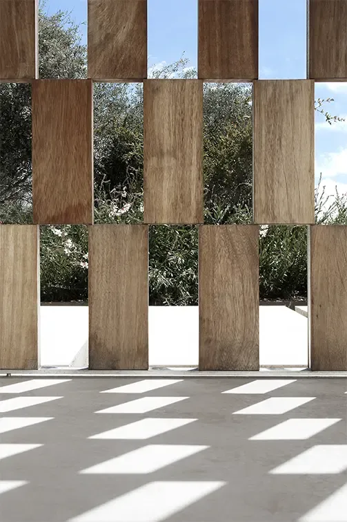 Close-up of wooden lattice facade with sunlight casting geometric shadows on the terrace floor.