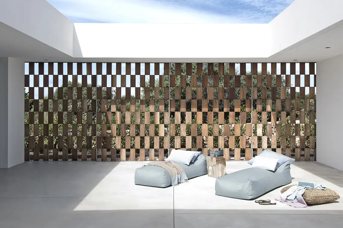 Minimalist patio with wooden lattice wall, loungers, and natural light creating relaxing Mediterranean atmosphere.