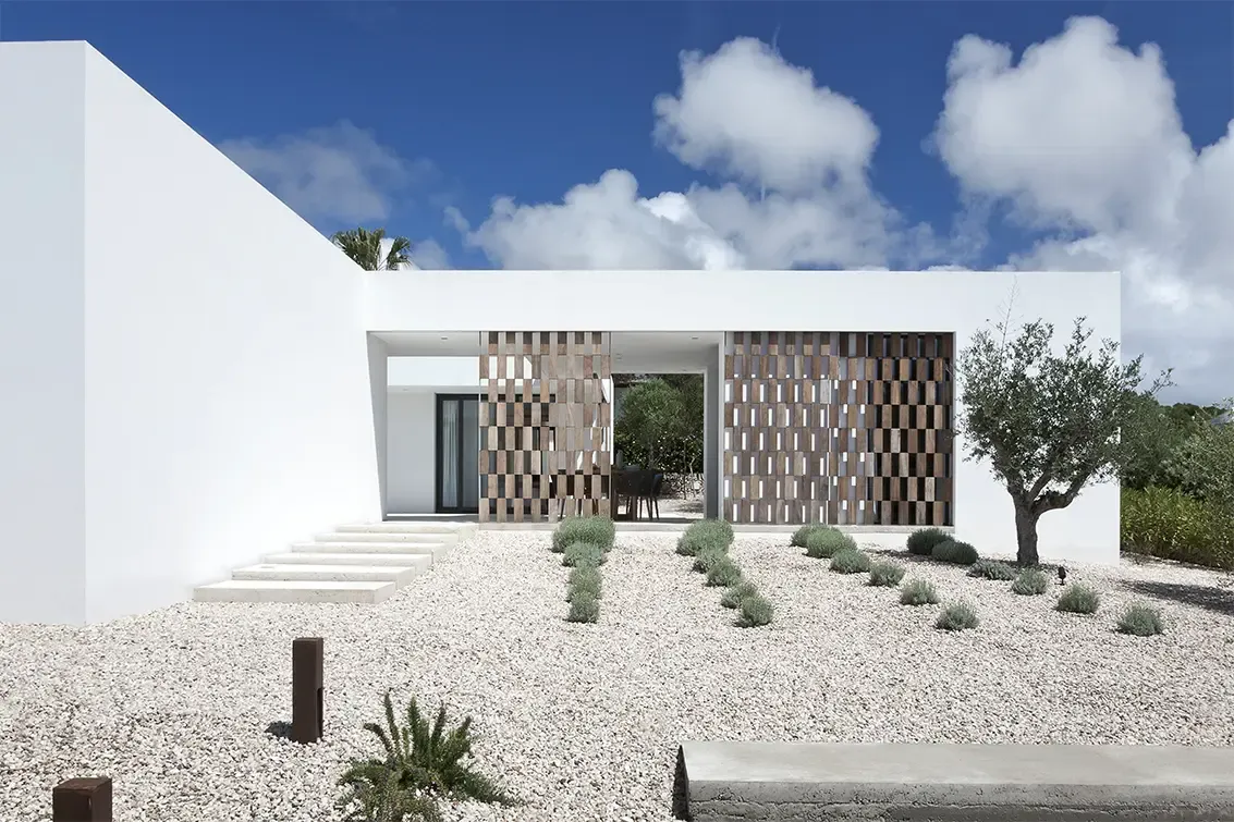 Symmetrical front view of minimalist white house with lattice panels and landscaped gravel garden.