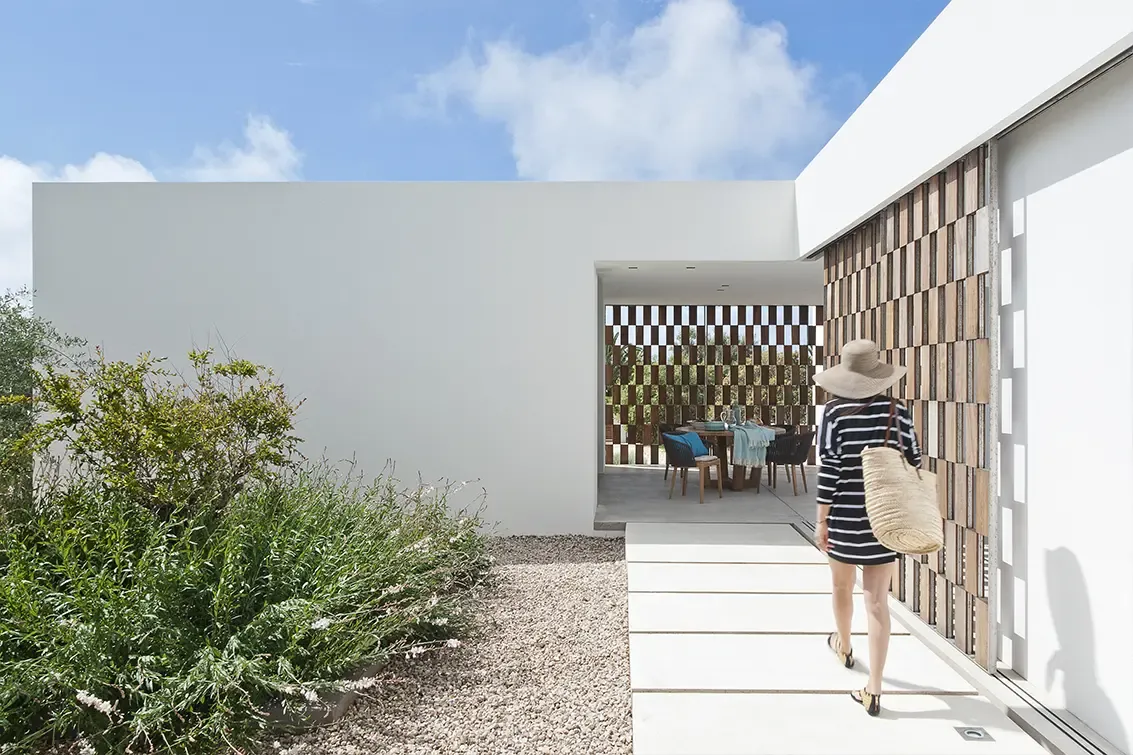 Pathway leading to covered dining terrace framed by lattice walls, with woman in striped dress entering.