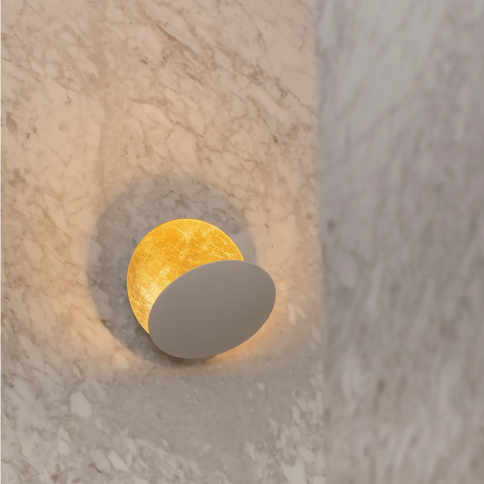Sculptural wall light with golden interior mounted on textured marble, creating a warm ambient glow.