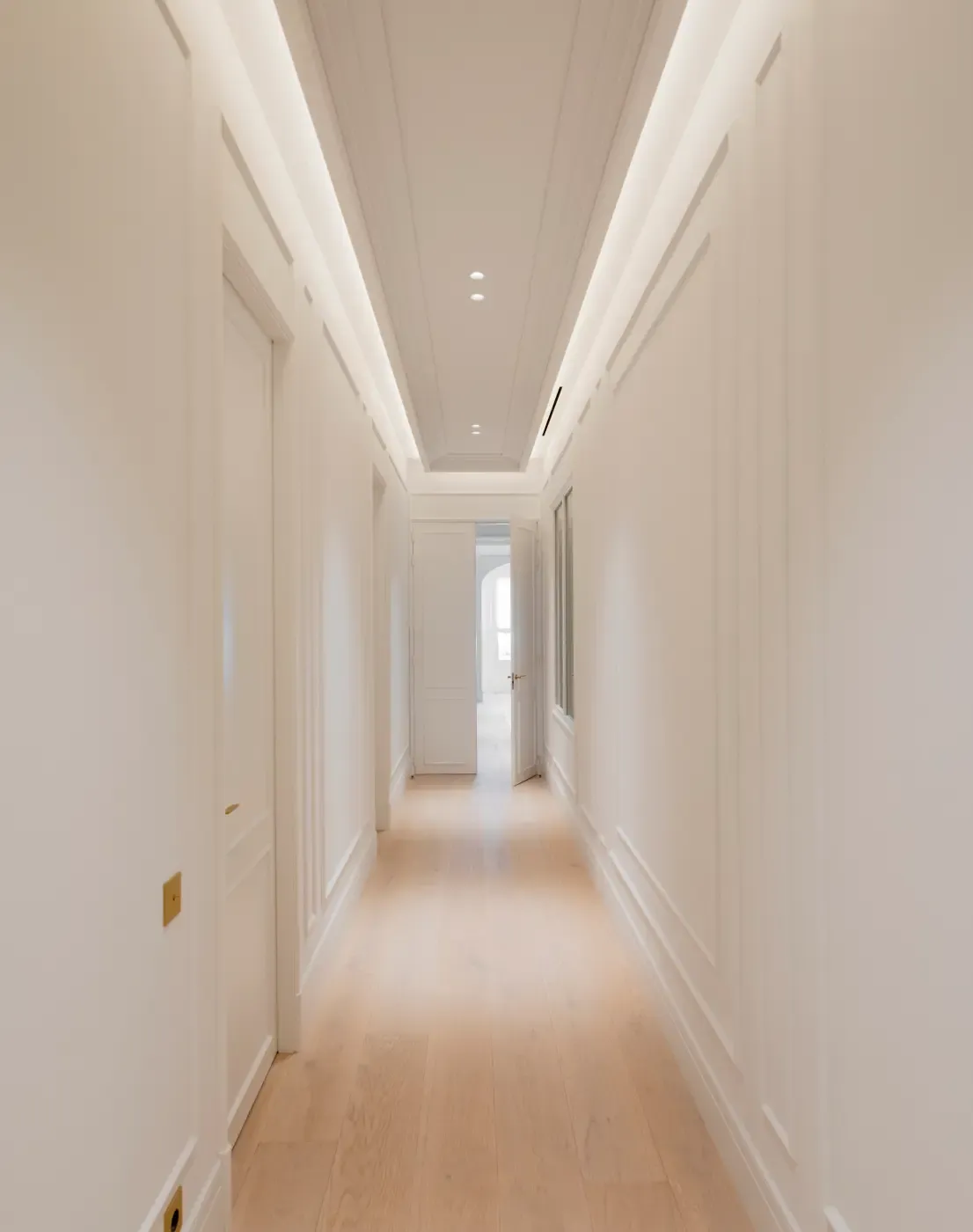 Minimalist hallway with decorative molding, oak flooring, and integrated ceiling lighting in a serene luxury apartment.