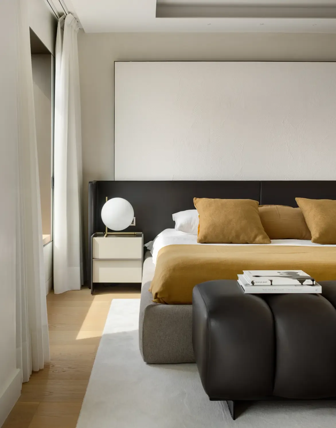 Contemporary bedroom with warm textiles, leather bench and minimalist bedside lighting